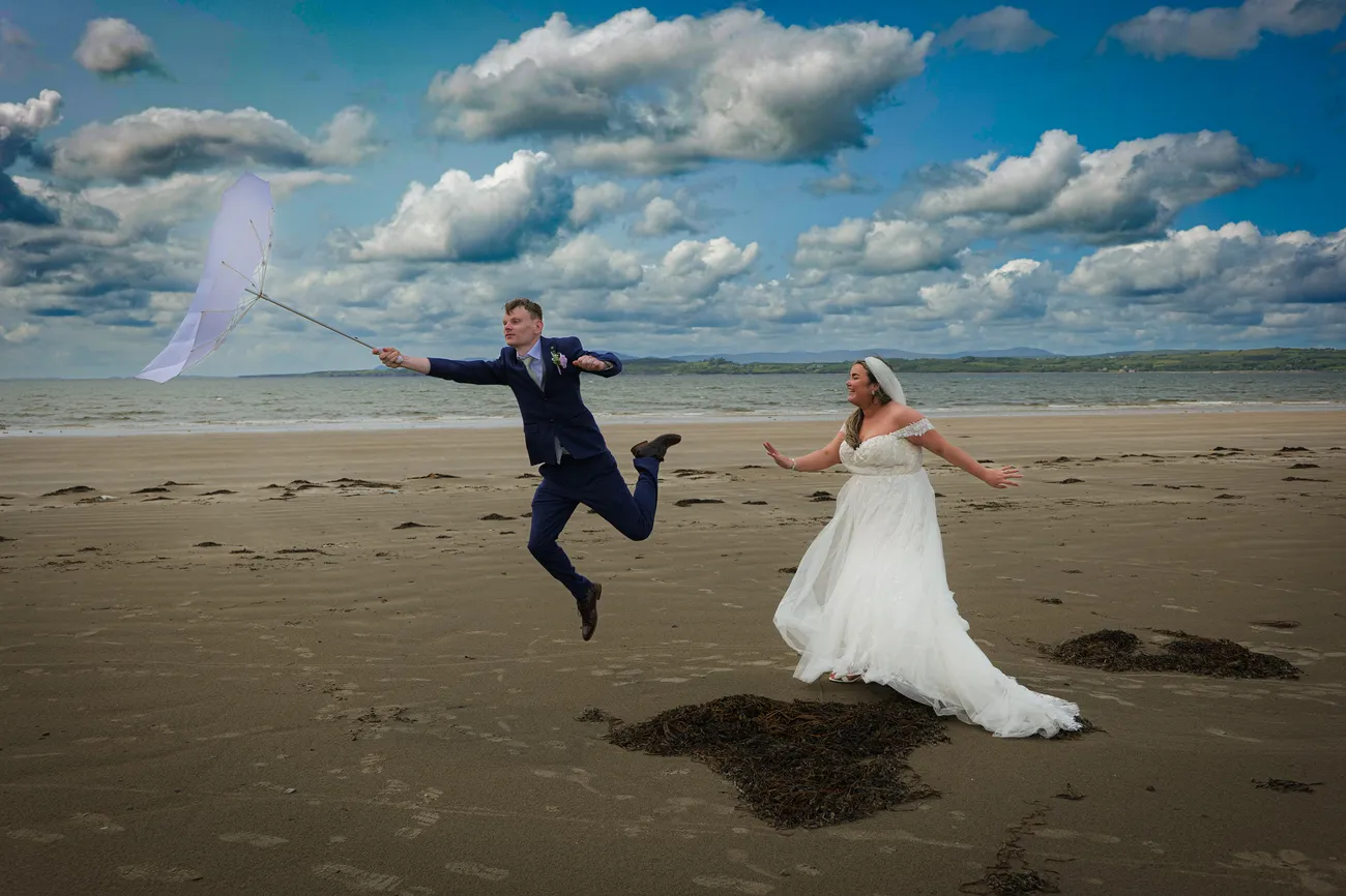 Fun beach portrait as a groom tosses a veil into the air