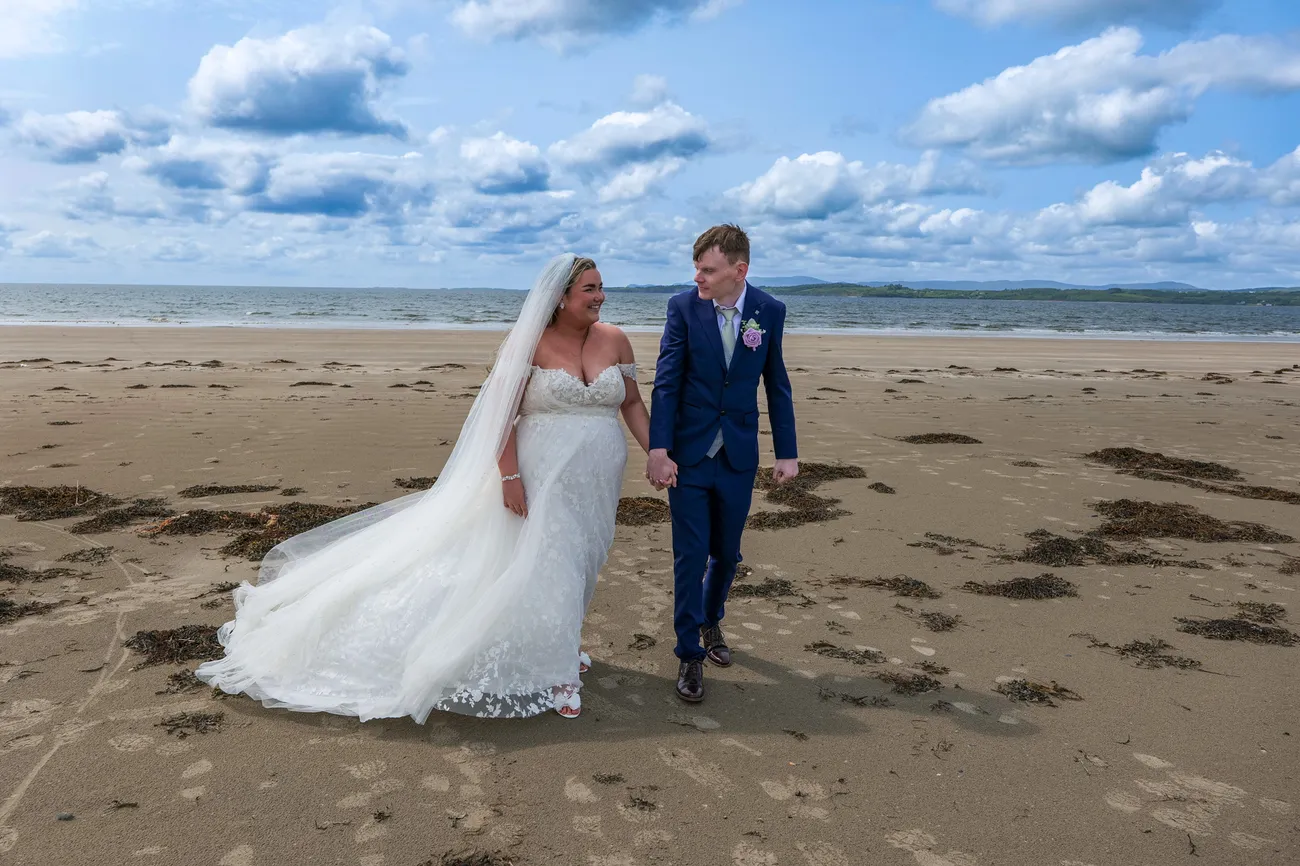 Newlyweds walking on a beach below a cloudy sky