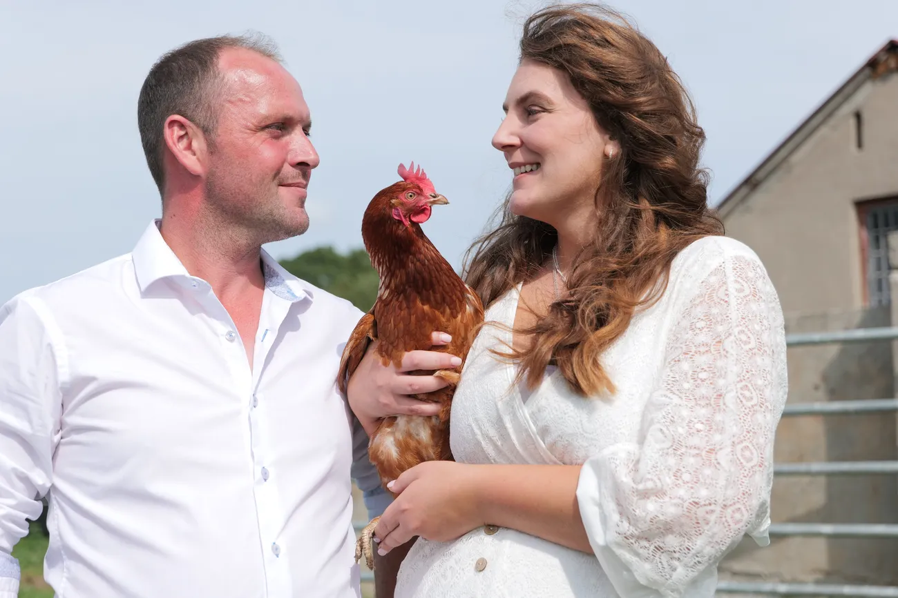 Bride holding a hen beside the groom at a farm wedding