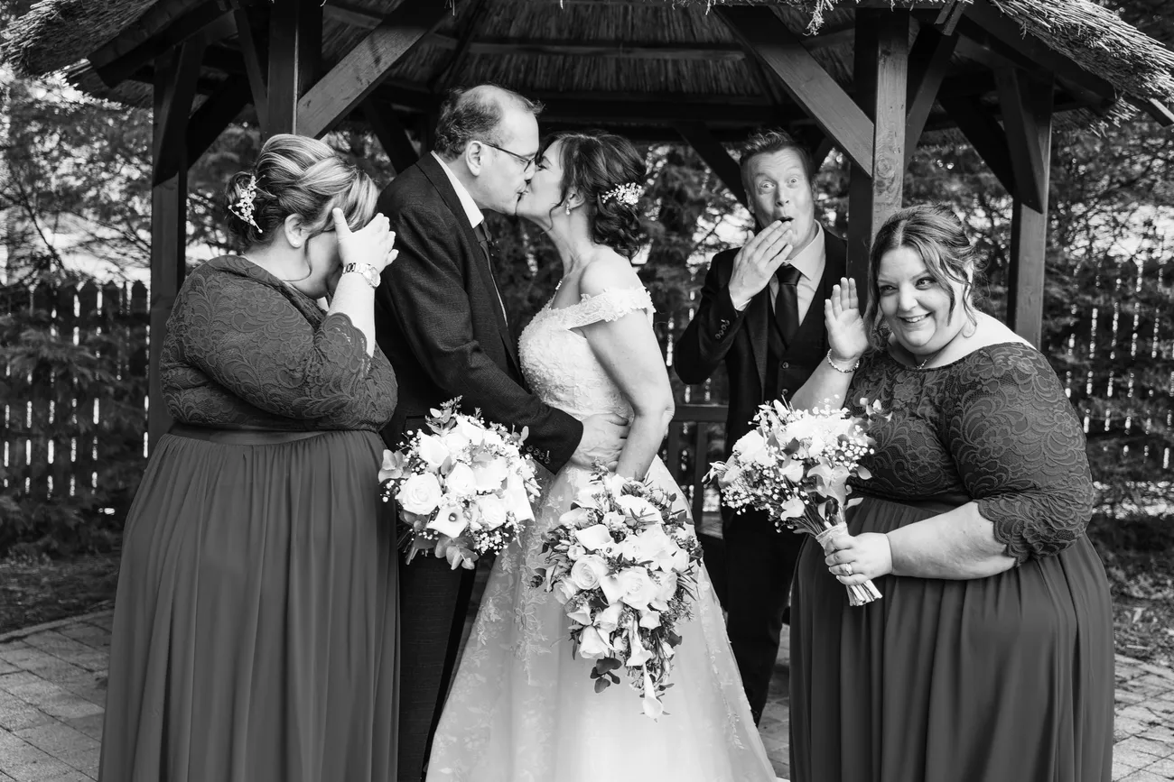 Bride and bridesmaids laughing under a gazebo in black and white