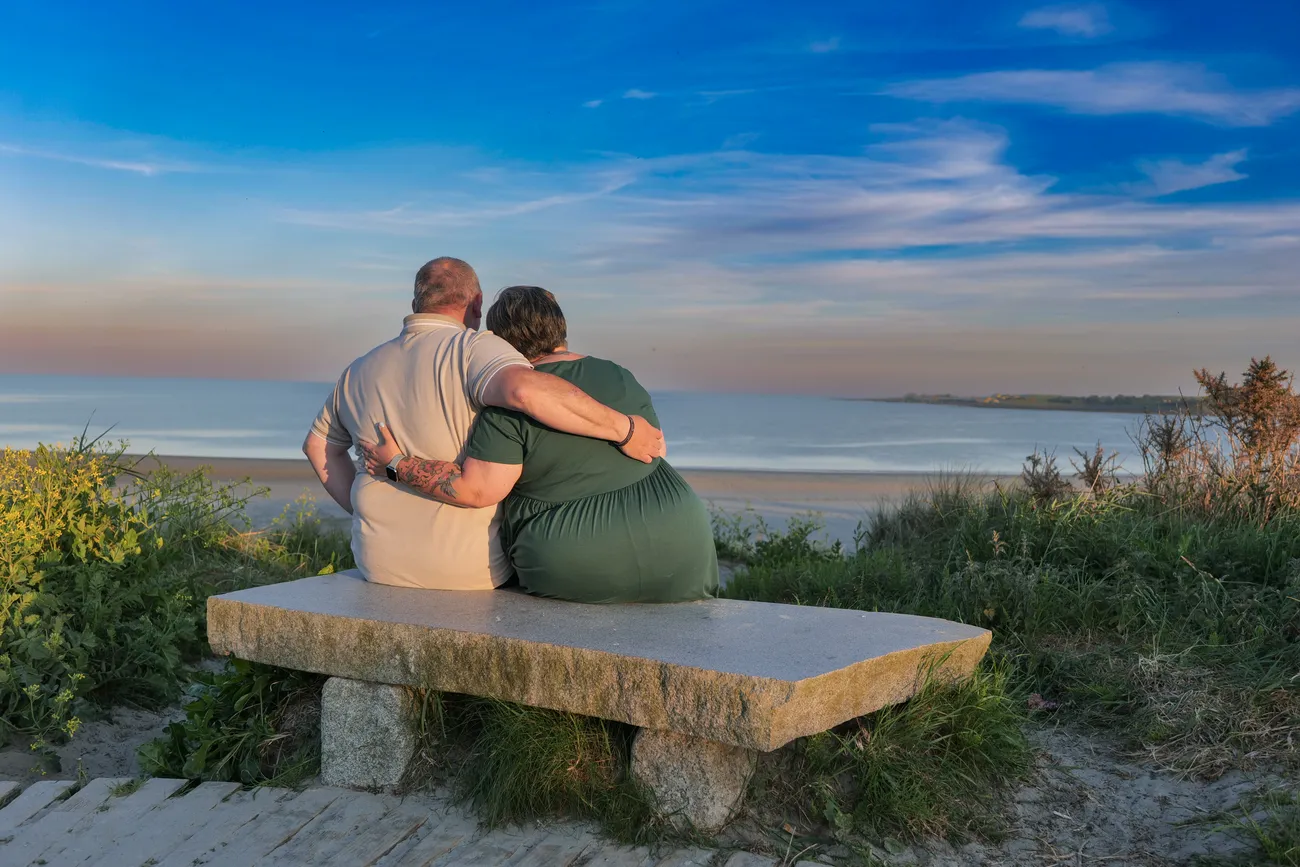 Couple sitting together on a bench above the coast