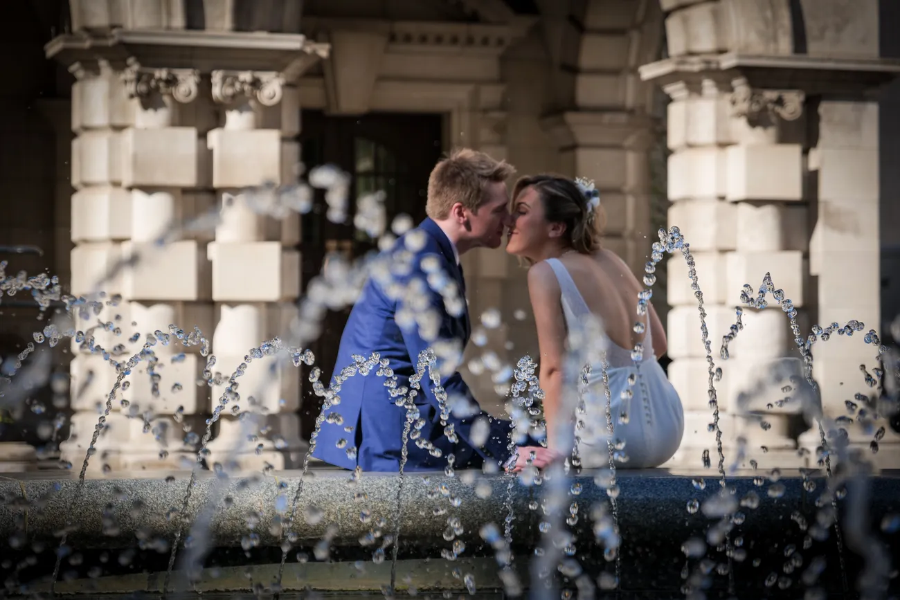 Newlyweds kissing beside a fountain and stone terrace