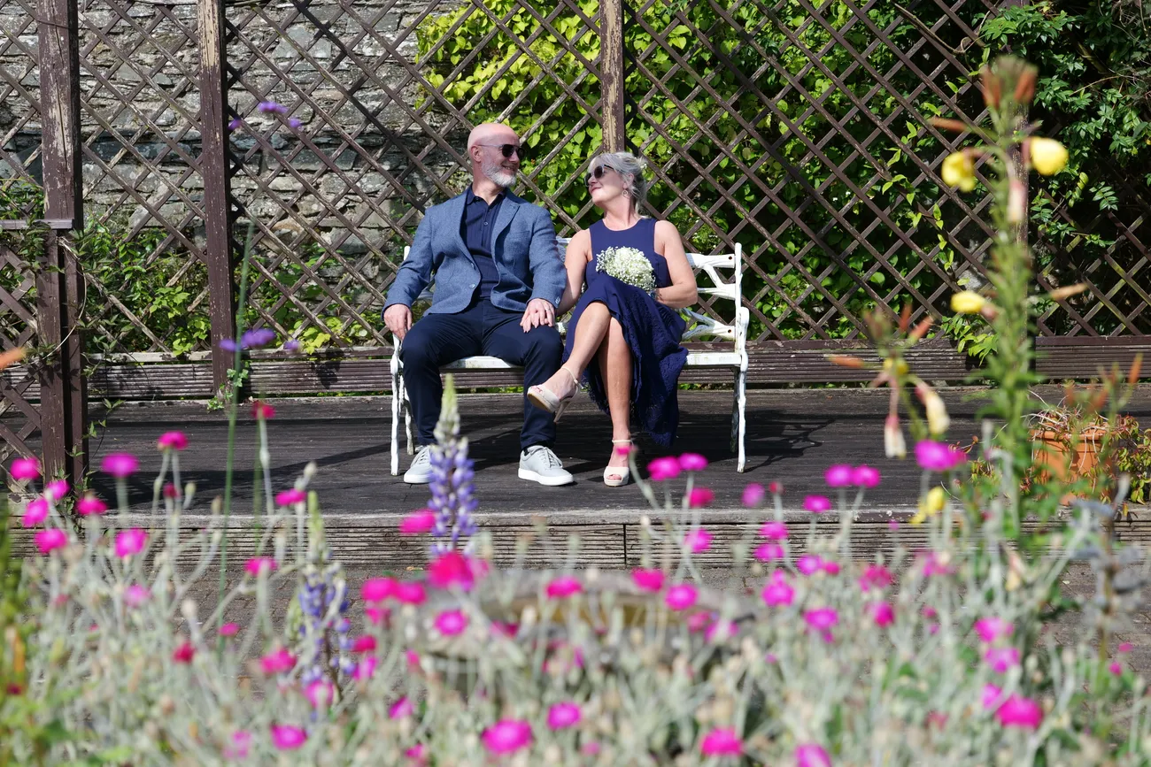 Wedding guests seated on a garden bench behind flowers
