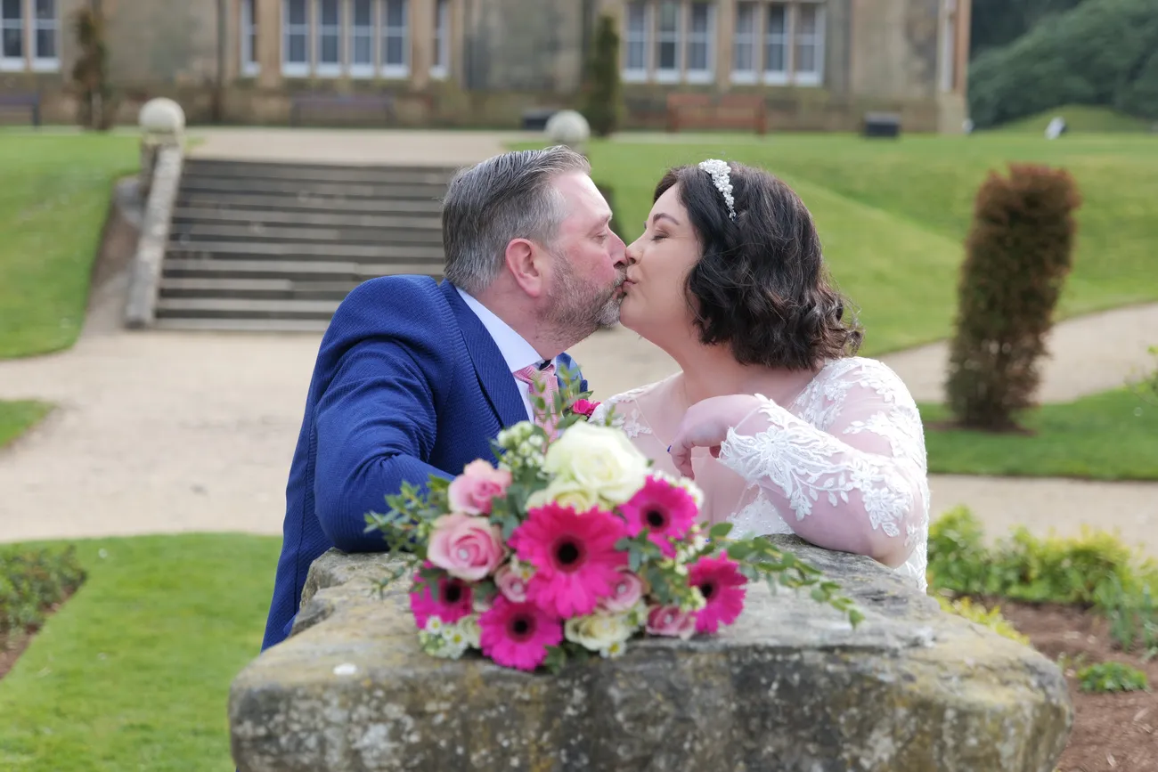 Garden wedding kiss behind a bright bouquet