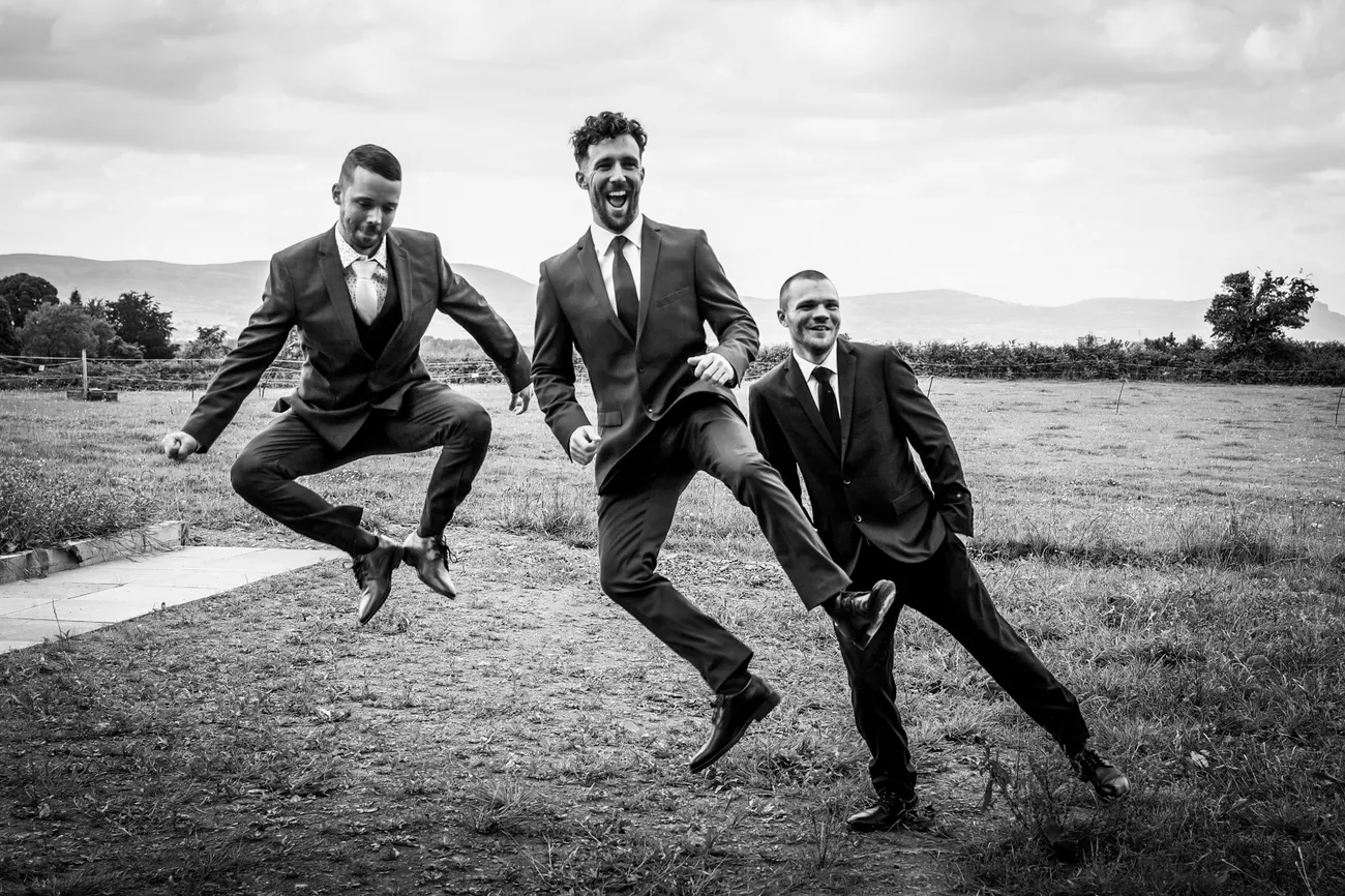 Groomsmen jumping in a field in black and white