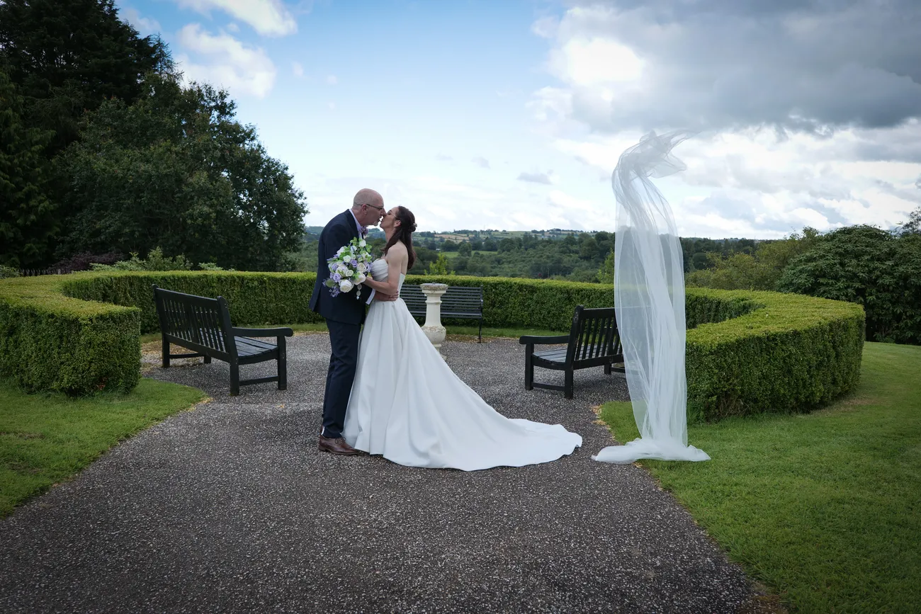 Garden wedding portrait with a veil blowing across a hedge view