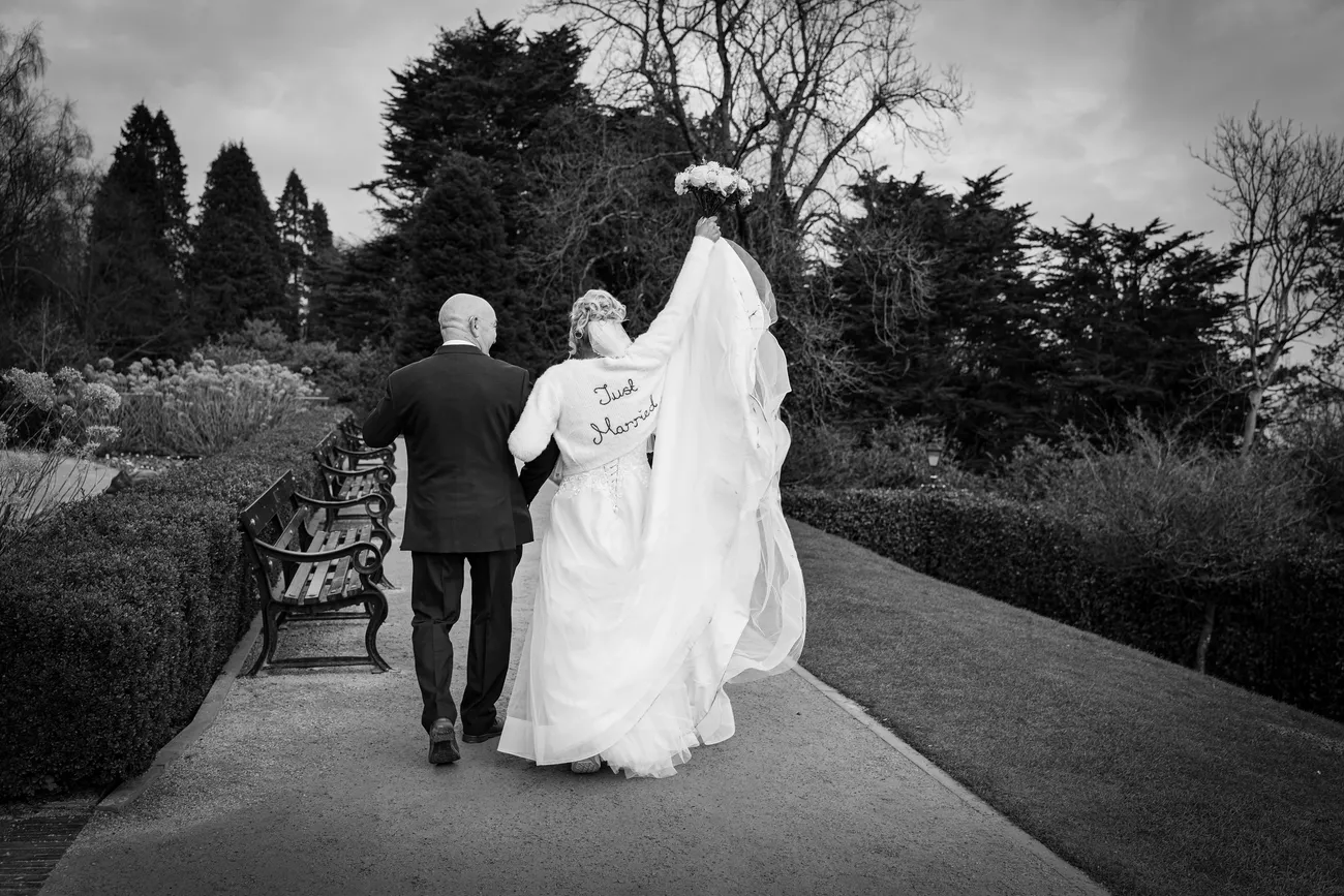 Newlyweds walking down a path with veil lifted in black and white