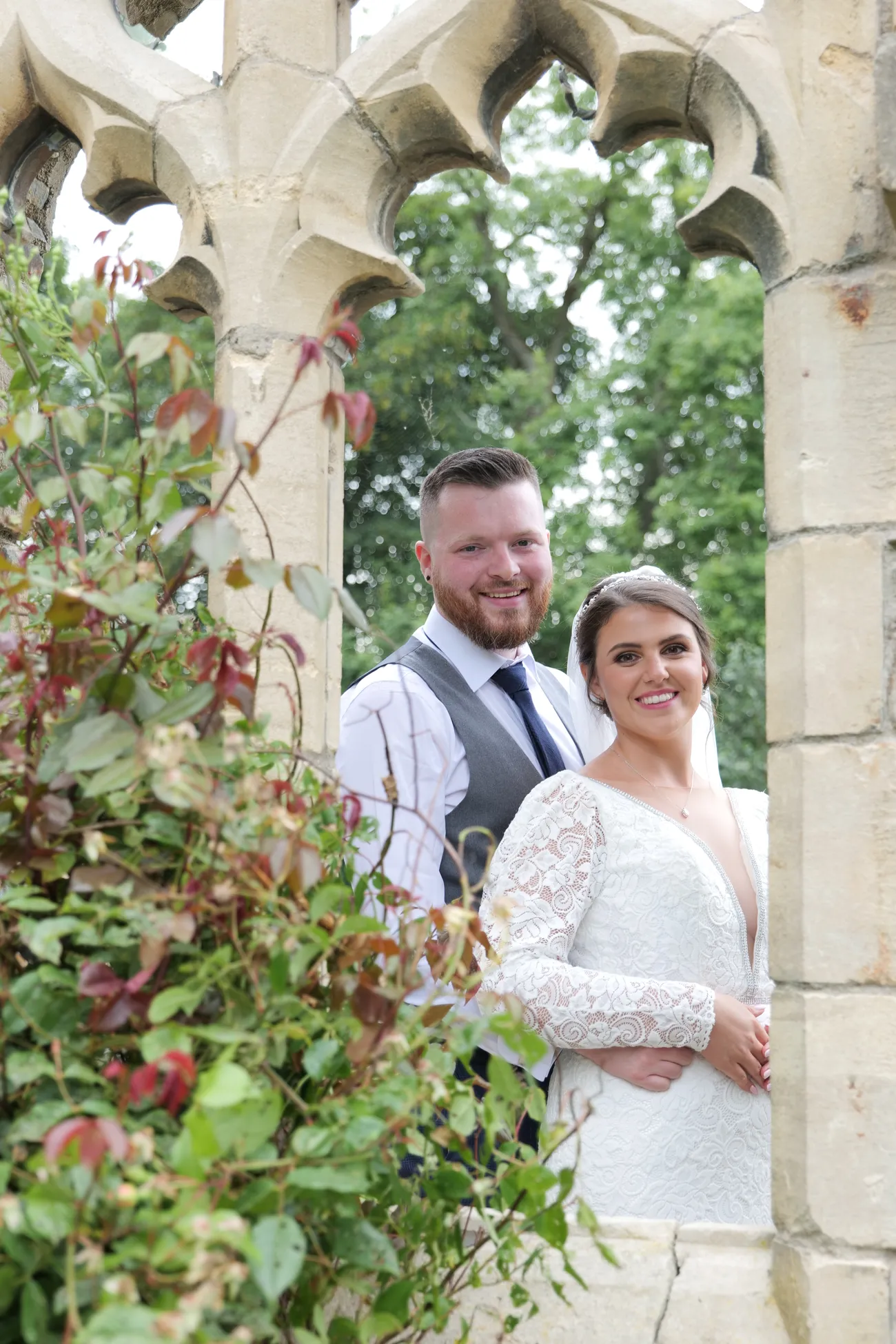 Couple portrait framed by a rose-covered stone arch